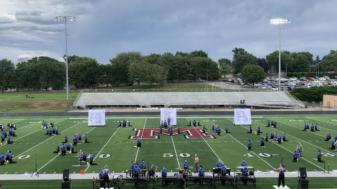 Marching band show with three square backdrops in the back. They each have a grey comic 
                        panel with respective black and white sketches of a flute player, a clarinet player, and a flag being 
                        tossed in the air.