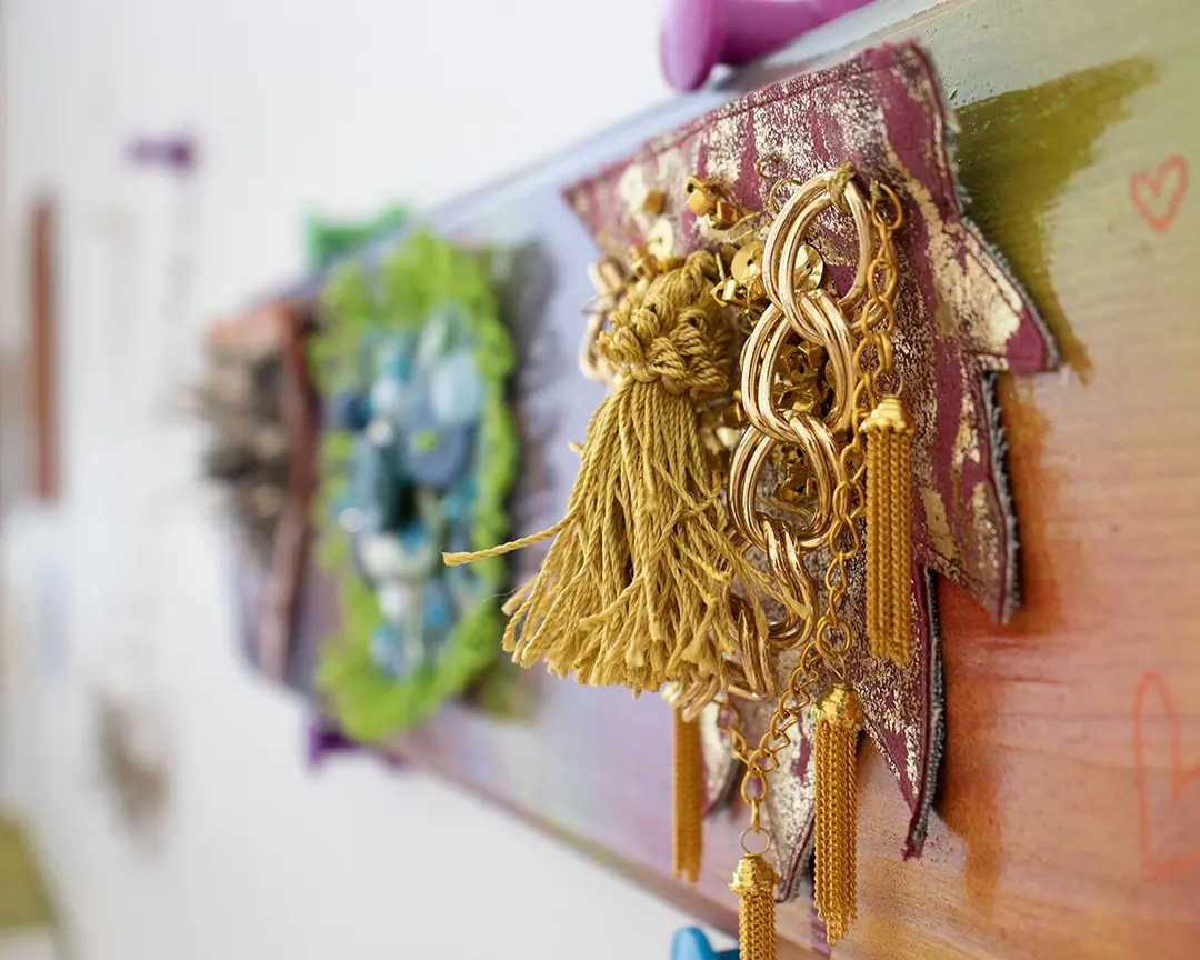 3/4 view of the gold bush mounted on a colorful board. The edges of the bush 
                        are spiked and it has layered gold tassels and chains on it. Two other bushes on the 
                        board are out of focus in the background.