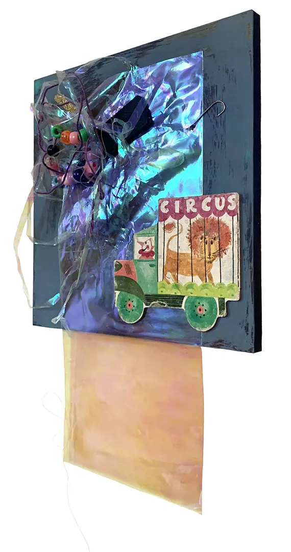 Right angle view of a three-dimensional collage on a painted board. It's made of miscellaneous 
                            trash, including strings of beads, plastic, and a circus cutout from a children's book.