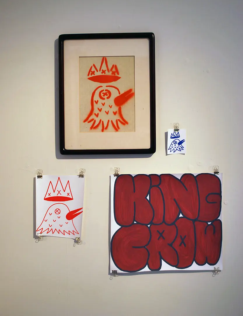 Close up of right wall in photo corner. There's one framed print of a crow with a crown, 
                            a large and small sticker with the same image, and a large sticker that says 'KING CROW'.