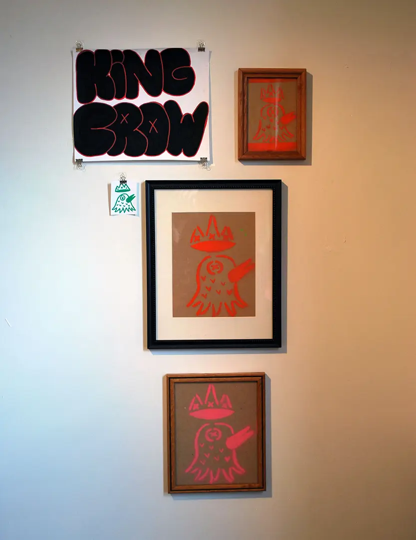 Close up of left wall in photo corner. There's a large format sticker that says 
                            'KING CROW'. There are three framed cardboard prints of a crow with a crown and a small sticker 
                            with the same image.