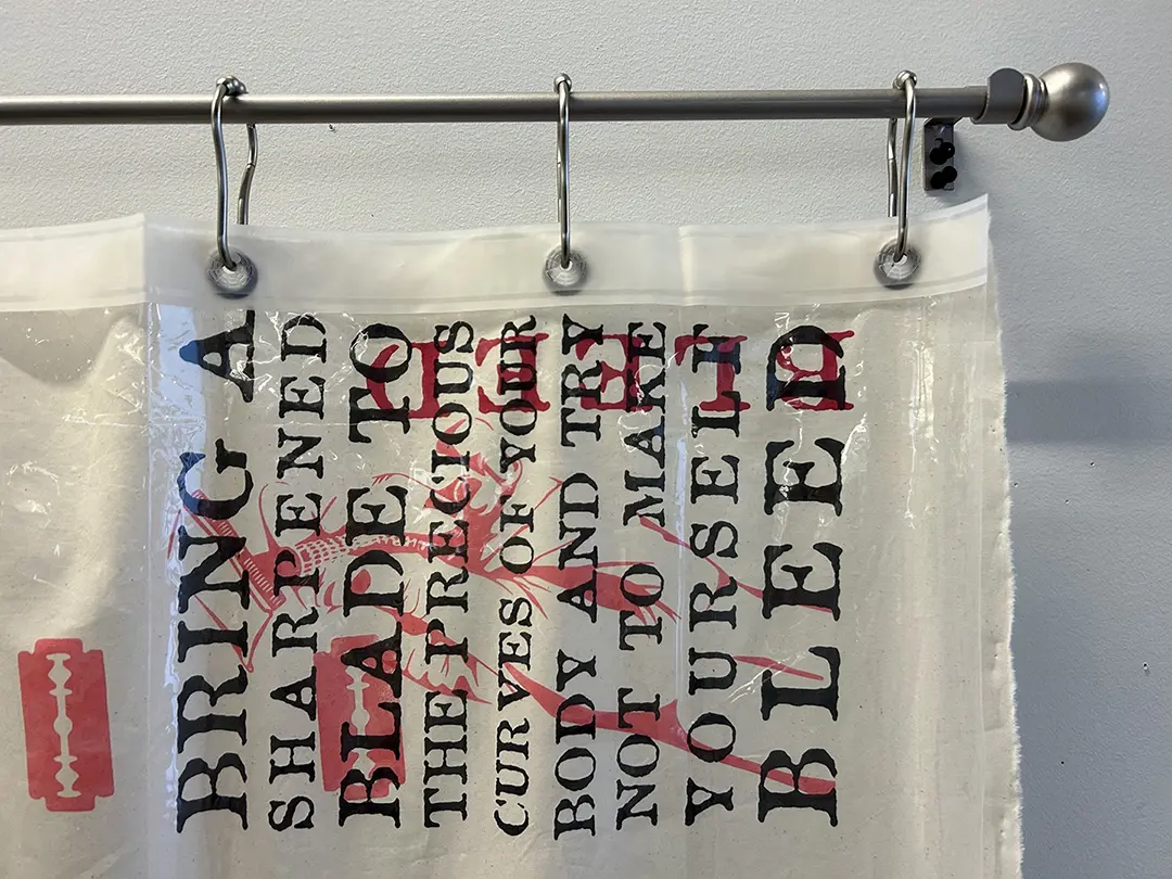 Close up of the top corner of the curtain. The text reads "Bring a sharpened 
                            blade to the precious curves of your body and try not to make yourself bleed." 
                            The text is printed sideways and layered with images of razor blades.