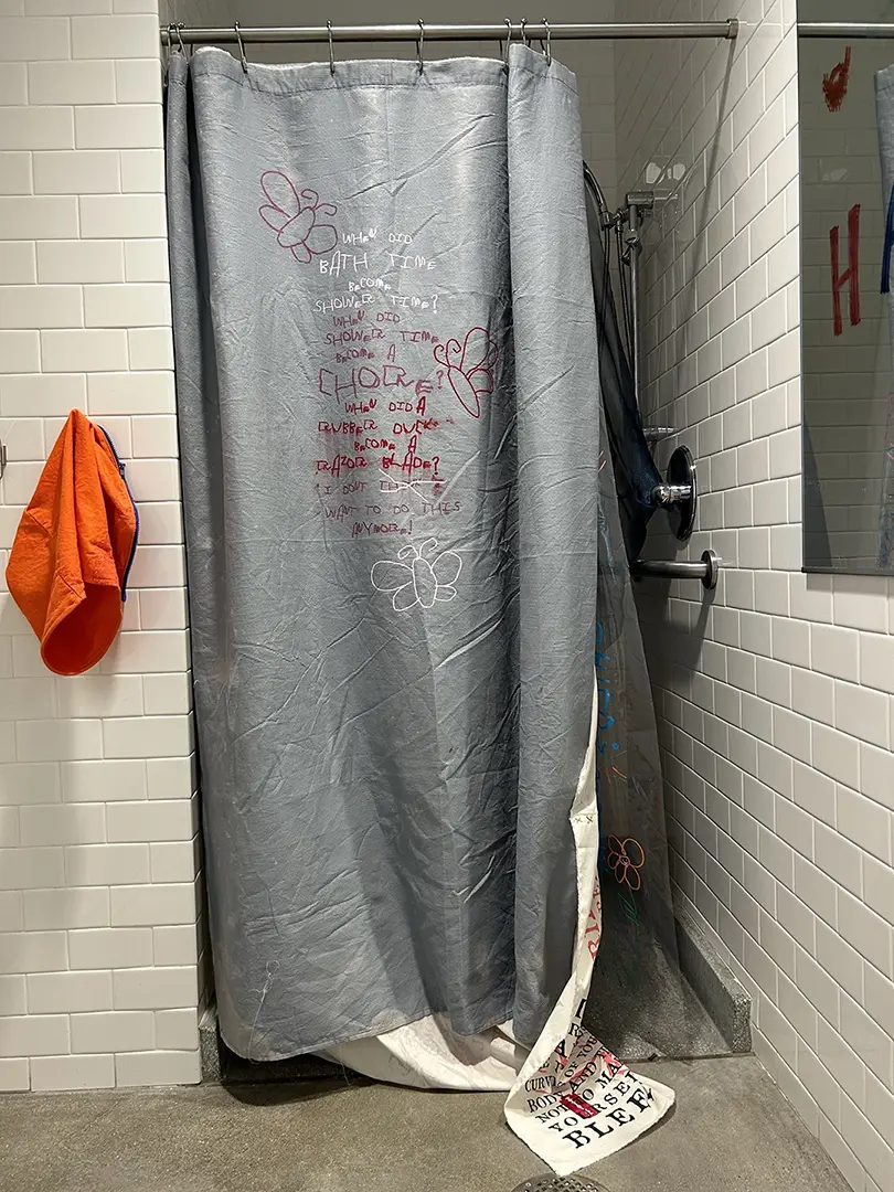 Shower with curtain slightly open. On the outer curtain is a poem printed in pink and red ink.