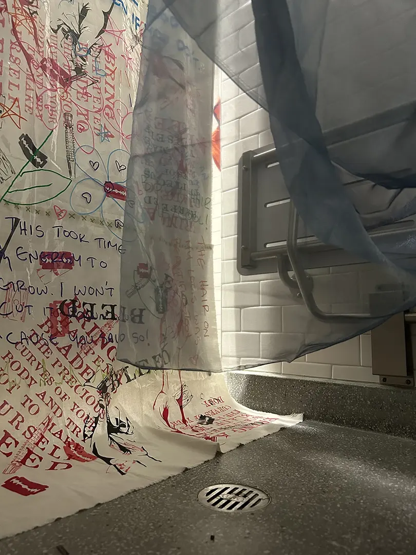 The bottom part of the curtain from inside the shower. The blue sheer fabric is draped partially 
                            in front of the camera.