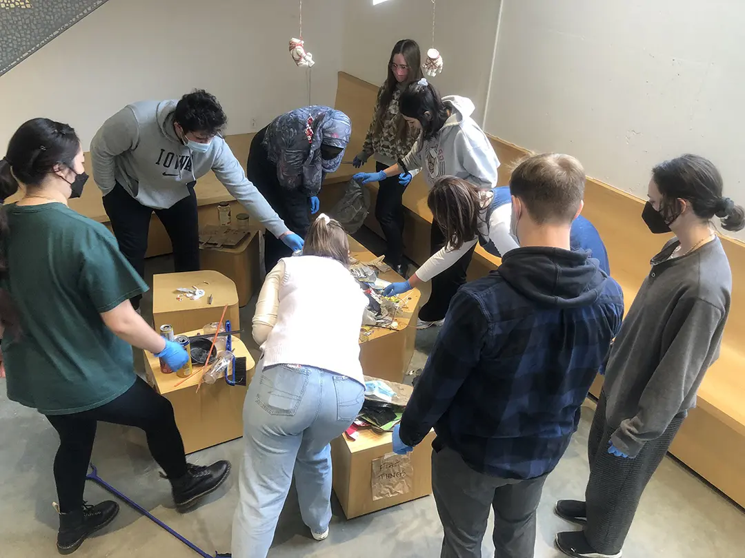 Still from a video of 'Sort Trash With Me!' Kate and their classmates are 
                        sorting trash that has been dumped on a pedestal in the Visual Arts Building.