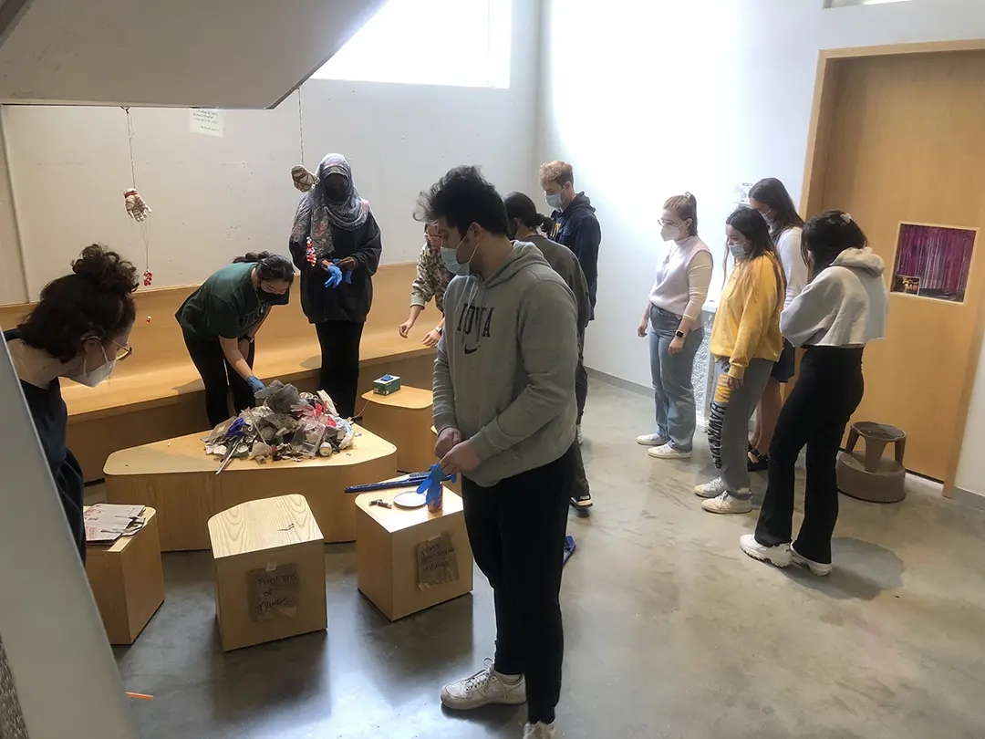 Still from a video of 'Sort Trash With Me!' Kate and their classmates are 
                        sorting trash that has been dumped on a pedestal in the Visual Arts Building.